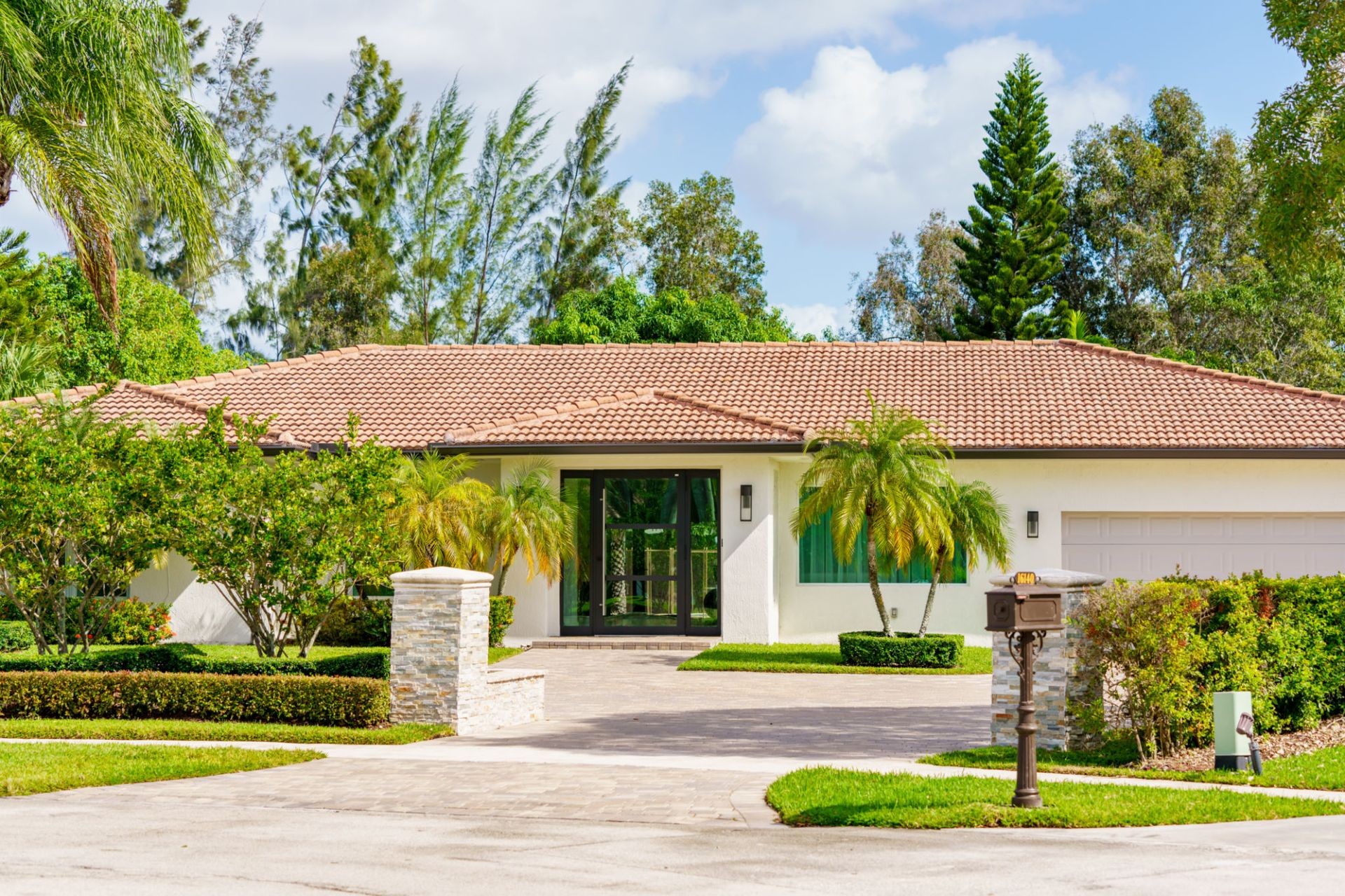 Single-story house with a tile roof, surrounded by palm trees and greenery.