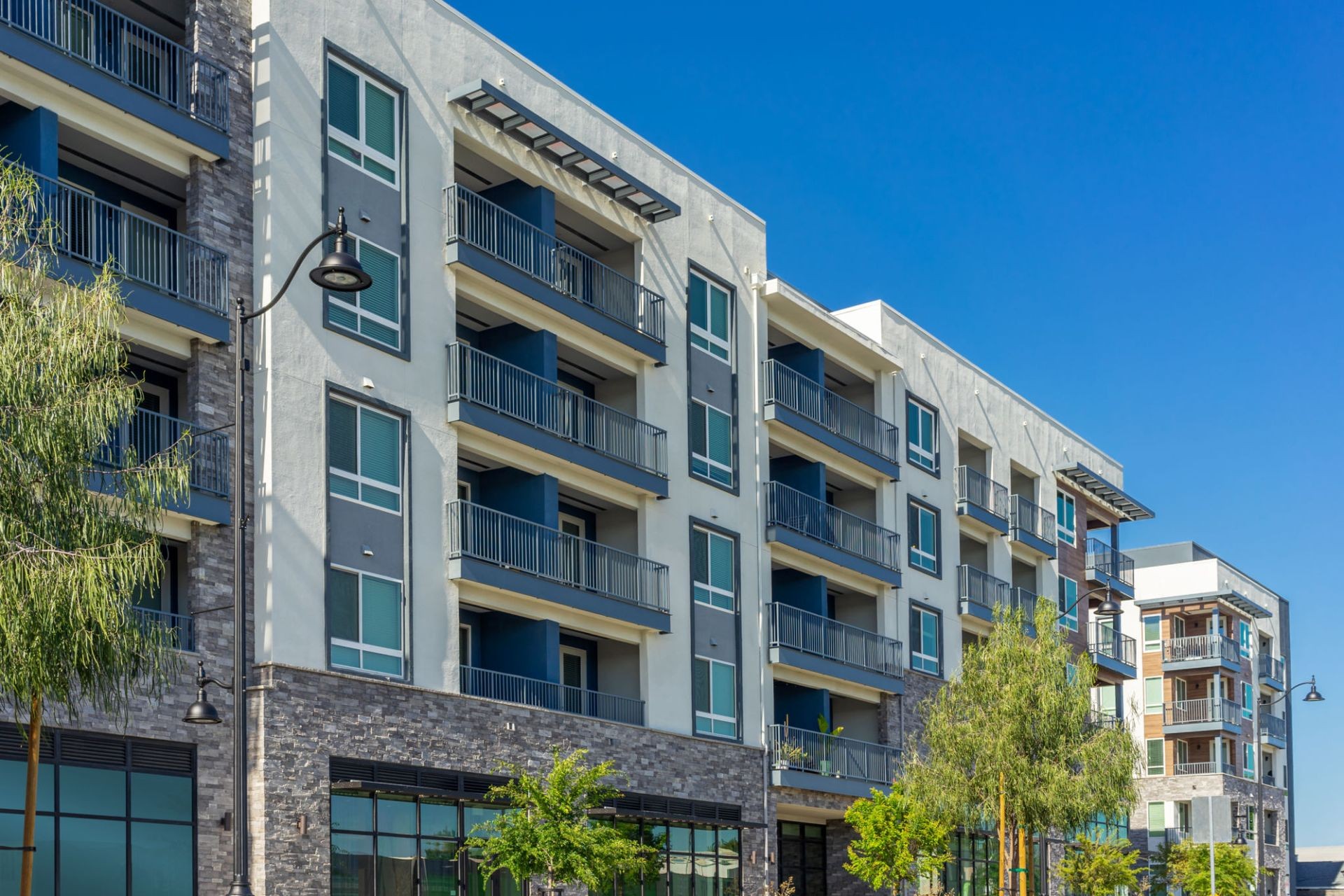 Modern multi-story apartment building with balconies and large windows, set against a clear blue sky.