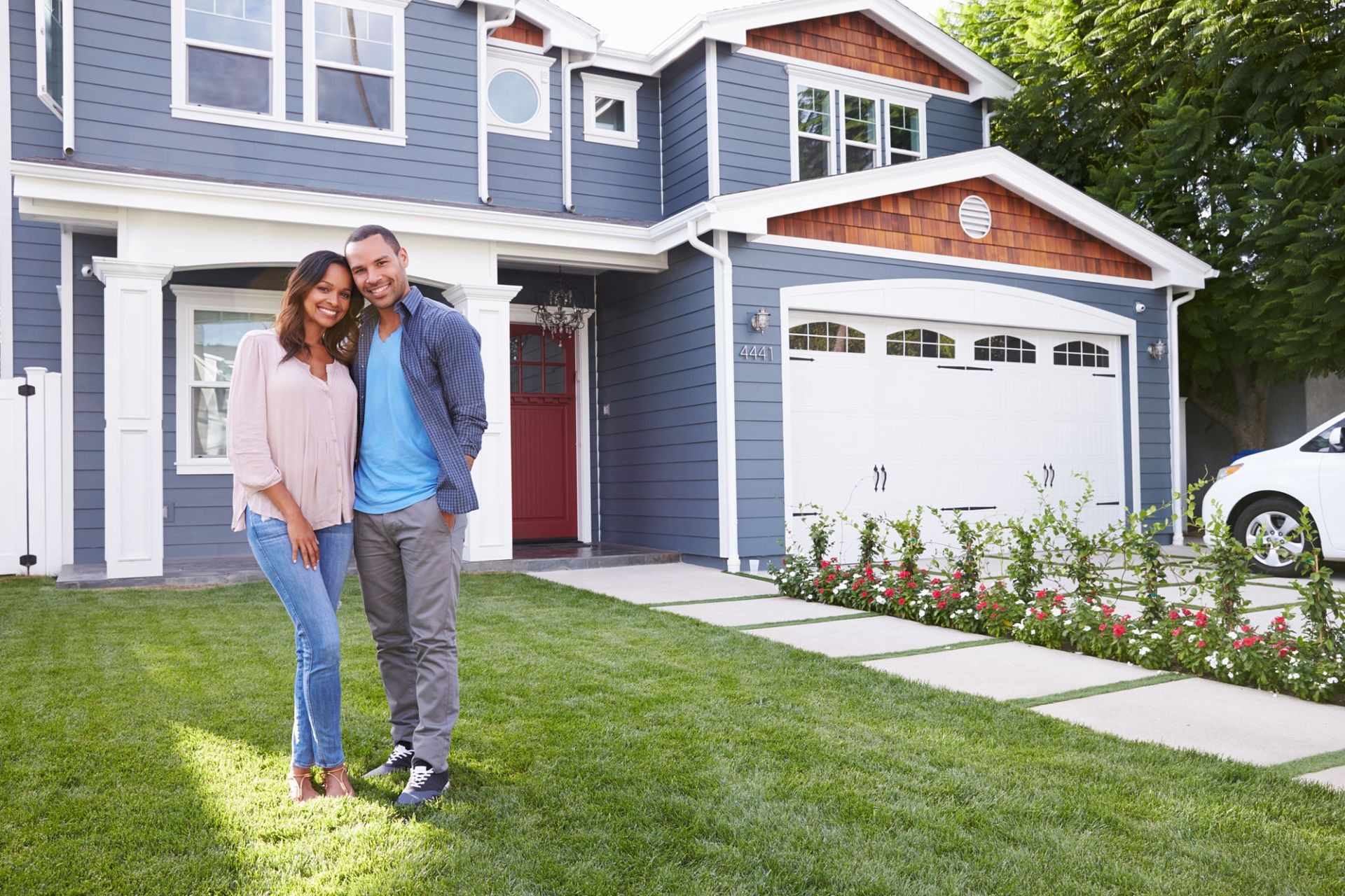 Smiling couple standing on a lawn in front of their modern suburban home with a garage.