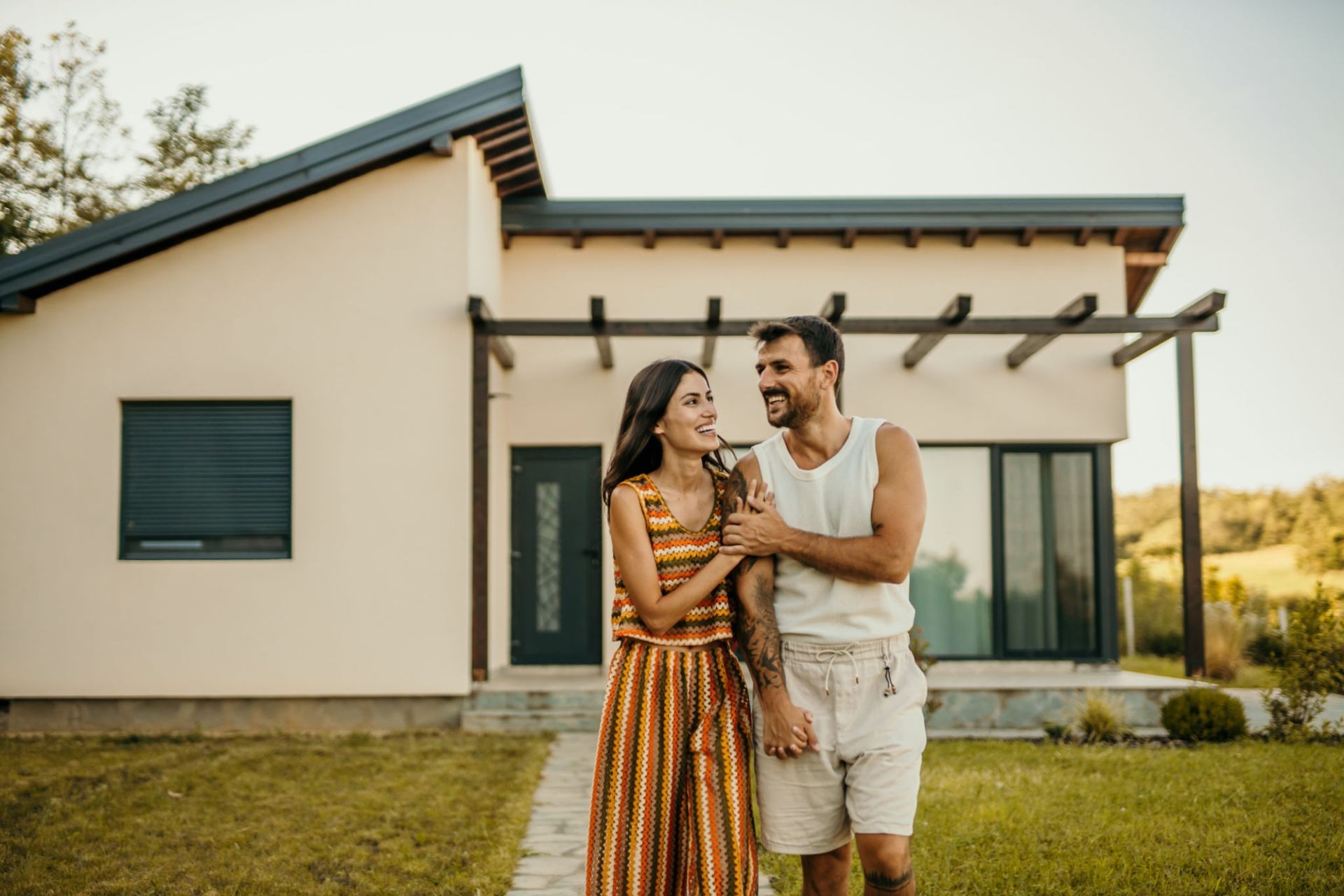 Couple smiling and walking in front of a modern house with green lawn.