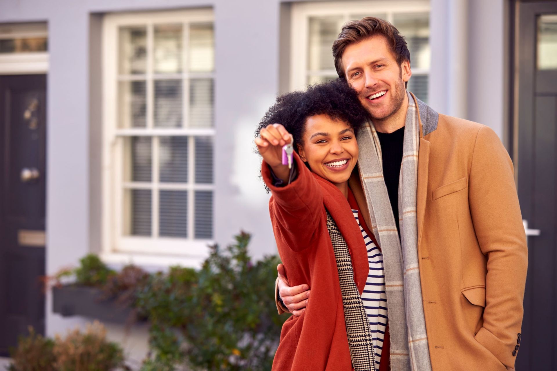 Happy couple standing outside their new home, holding a set of keys.