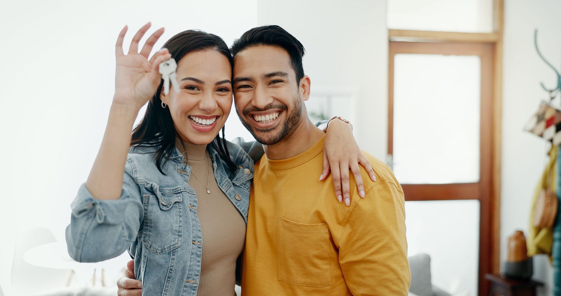 Smiling couple holding keys in a bright room, symbolizing a new home or apartment ownership.