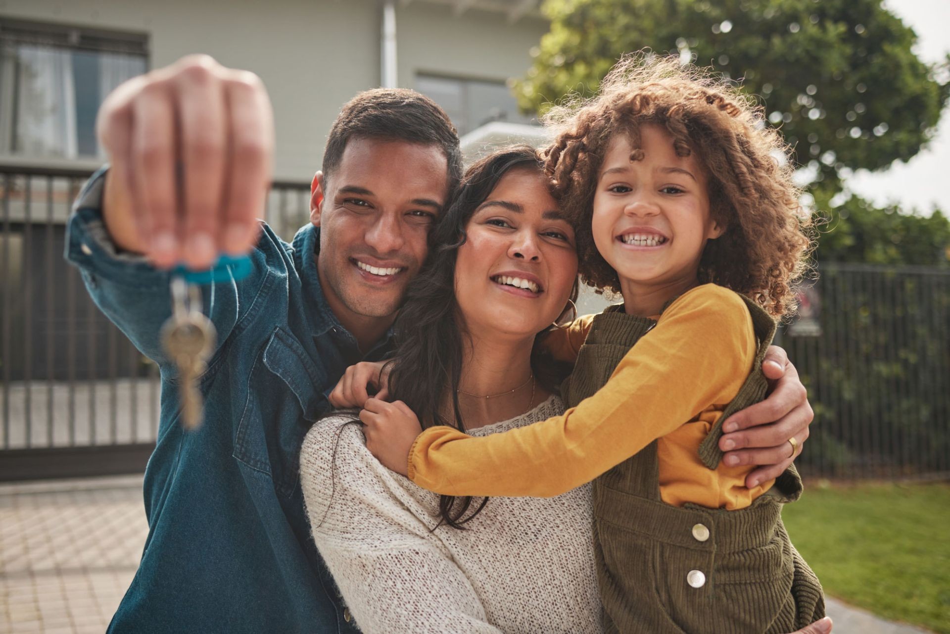 Smiling family holding house keys in front of a new home.