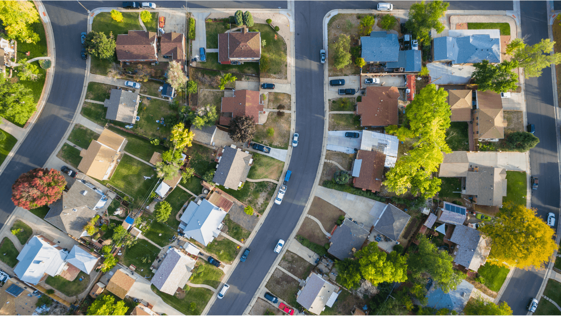 Aerial view of a suburban neighborhood with houses, green lawns, and tree-lined streets.