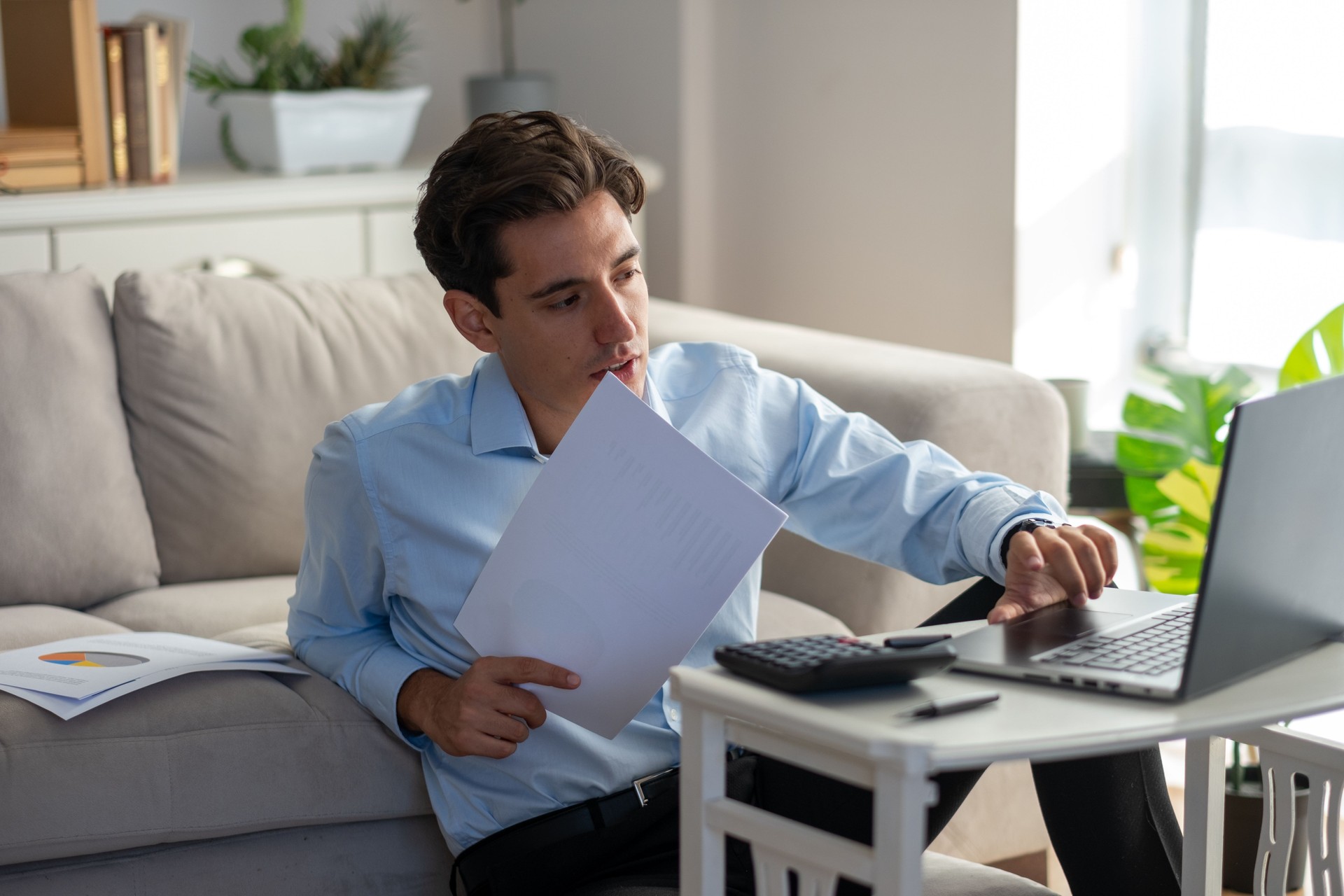 Focused young businessman working from home on laptop and documents