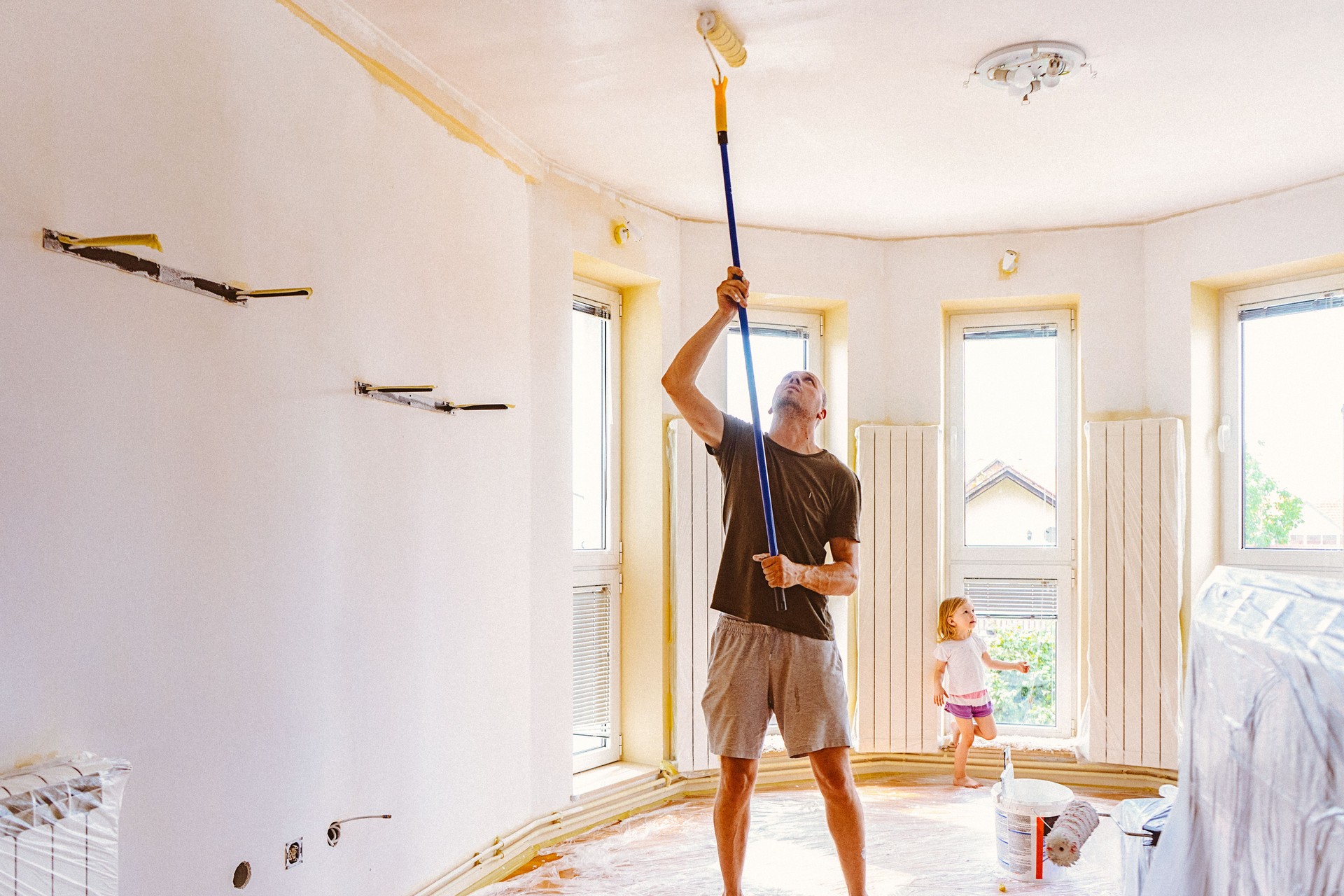 Young man painting ceiling with telescopic roller