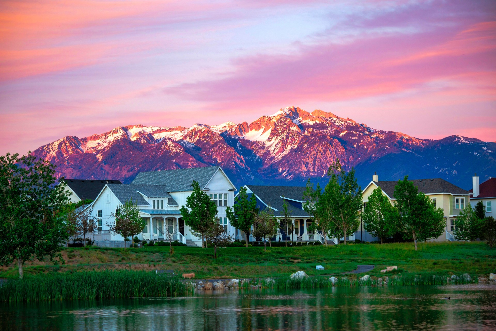 Scenic view of a mountain and houses with trees around them and a lake against it at the sunset