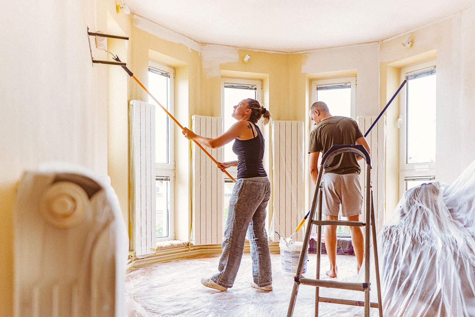 Couple painting wall and ceiling with telescopic roller